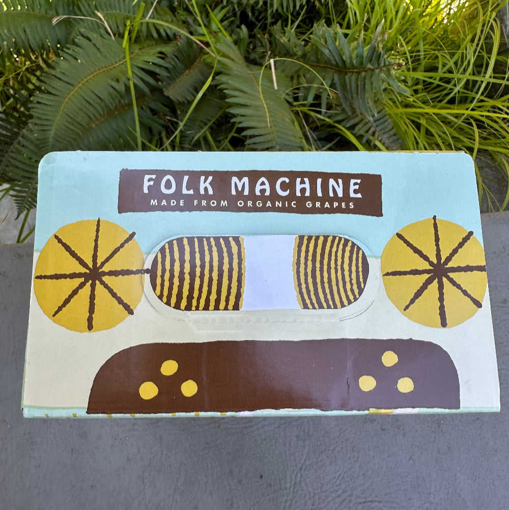 Product packaging with geometric design and 'Folk Machine' branding on a gray surface with green plants.