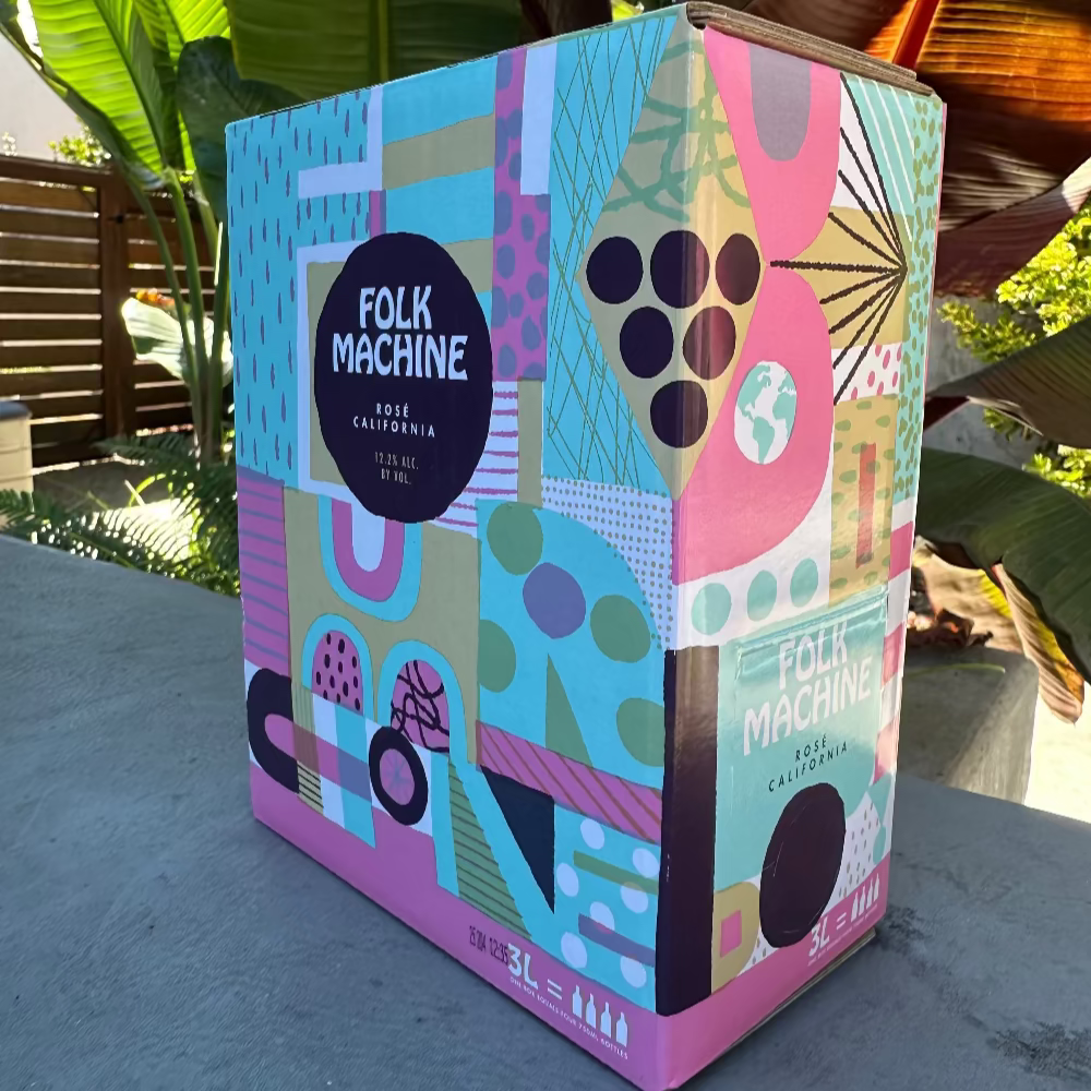 Colorful box with geometric patterns and 'Folk Machine' branding on a concrete surface with plants in the background.