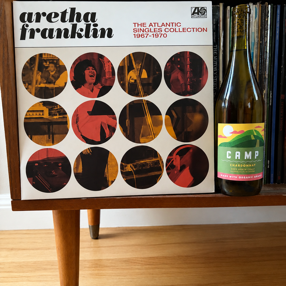 Aretha Franklin 'The Atlantic Singles Collection 1967-1970' vinyl record album displayed on a wooden shelf next to a bottle of Campagne red wine.
